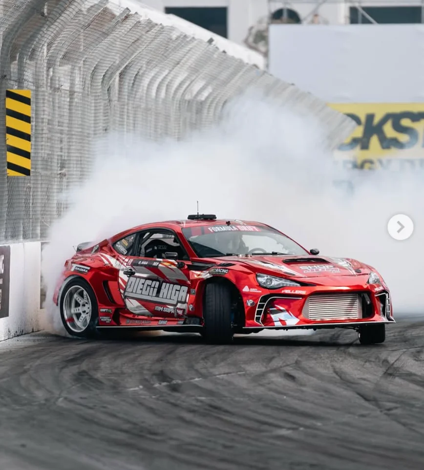 Diego Higa drifting his red race car close to a wall through tire smoke
